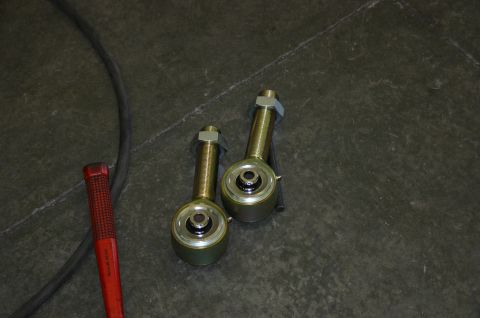 1995 Ford Bronco - Two gold suspension links with nuts and bearings are shown on a dark surface next to a red tool handle.