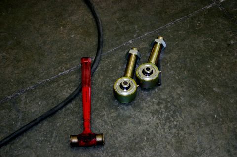 1995 Ford Bronco - Two suspension links and a red hammer are laid out on a textured floor, suggesting a repair or upgrade in progress.