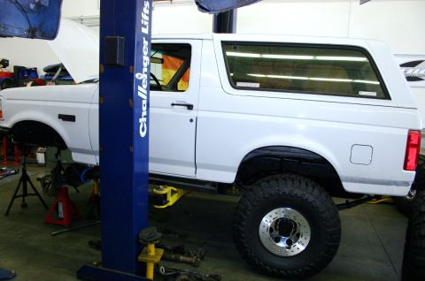 1995 Ford Bronco - A white SUV is raised on a hydraulic lift in a garage, with its hood open and suspension components visible.
