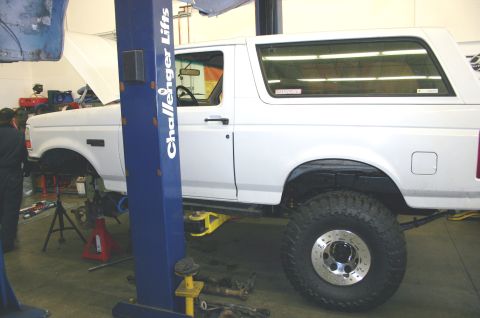 1995 Ford Bronco - A white SUV is undergoing maintenance in a garage, with its front end elevated on a hydraulic lift.