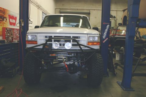1995 Ford Bronco - Front view of a 1995 Ford Bronco modified with a custom bumper and winch, parked in a repair shop.