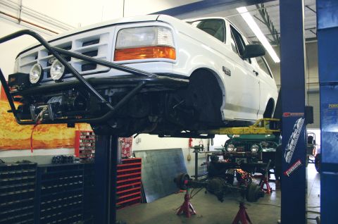 1995 Ford Bronco - A white SUV is raised on a lift in a garage, showing its undercarriage and a custom front bumper with a winch.