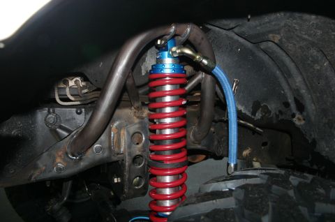 1995 Ford Bronco - Close-up of a modified front suspension system a red coilover shock absorber and blue braided hydraulic line.