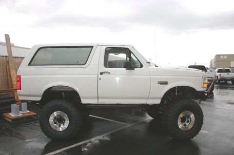 1995 Ford Bronco - A white Ford Bronco with significant suspension lift and oversized tires is parked outdoors on a wet surface.