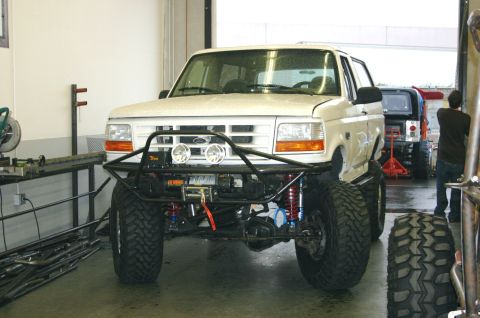1995 Ford Bronco - A white Ford Bronco is modified with a custom bumper and off-road tires, seen in a garage with another vehicle in the background.