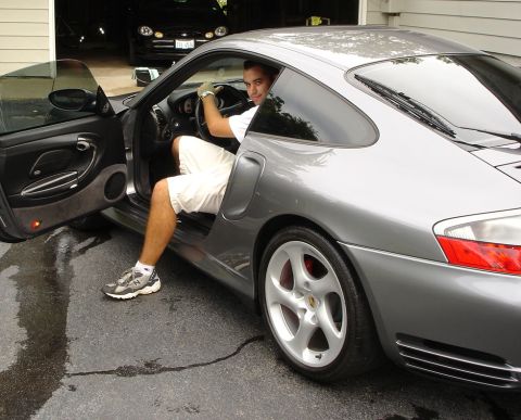 1998 Ford Taurus - A man enters a Porsche 911 parked in a driveway, with another vehicle visible in the background garage.