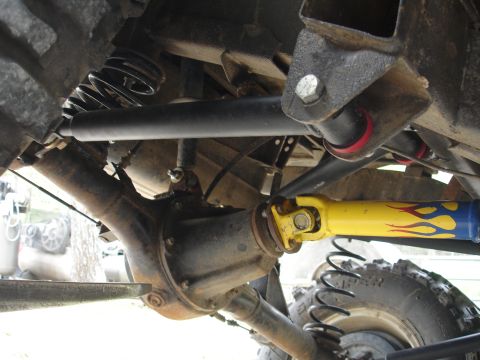 1987 Ford Bronco - Close-up of a vehicle's undercarriage, highlighting a custom yellow driveshaft with flame graphics and suspension parts.