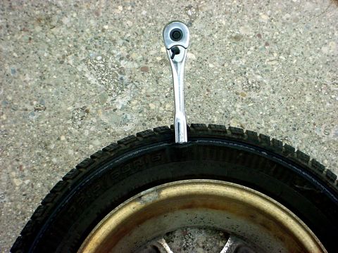 1973 Ford Ranchero - A socket wrench is lodged in the sidewall of a tire, resting on a concrete surface.