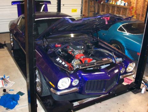 1970 Chevrolet Camaro - A purple 1970 Chevrolet Camaro is shown on a lift with its hood open, revealing the engine bay, while another car is visible behind it.