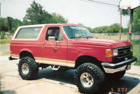 1990 Ford Bronco - This lifted 1990 Ford Bronco features a two-tone red and white paint scheme and aggressive off-road tires.