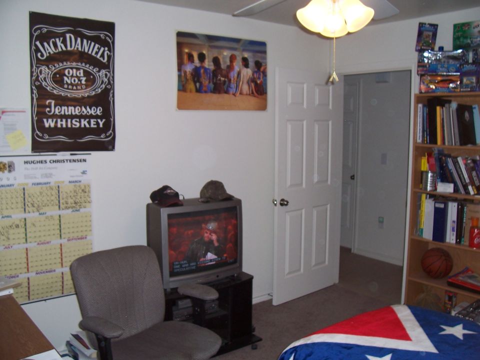 Room interior with Jack Daniels poster, artwork, calendar, TV, chair, and bookshelf