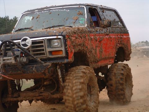 1993 Ford Bronco - This heavily mud-covered SUV, possibly a Ford Bronco, is equipped for off-road adventures with large tires and a winch. Another vehicle is…