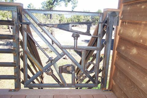 1990 Ford Bronco - This metal gate is decorated with various welded tools and mechanical parts, set against a wooden wall and outdoor scenery.