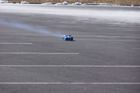 1994 Ford Bronco - A blue and white remote control car is seen drifting on an asphalt surface, emitting a trail of smoke.