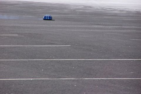 1994 Ford Bronco - A blue and white striped vehicle is seen from the rear on a wide asphalt surface.