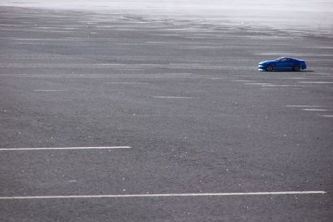 1994 Ford Bronco - A blue sports car is parked on a vast asphalt area with visible lane markings.