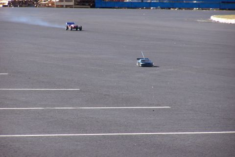 1994 Ford Bronco - Two radio-controlled cars race on a paved track, with one leaving a trail of smoke.