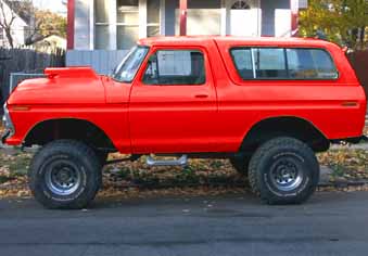 1978 Ford Bronco - A red 1978 Ford Bronco is shown from the side, a lifted suspension and an aftermarket hood scoop.