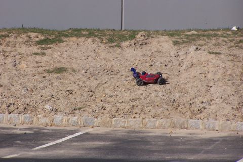 1994 Ford Bronco - A red remote control buggy is positioned on a dirt embankment next to a paved area.