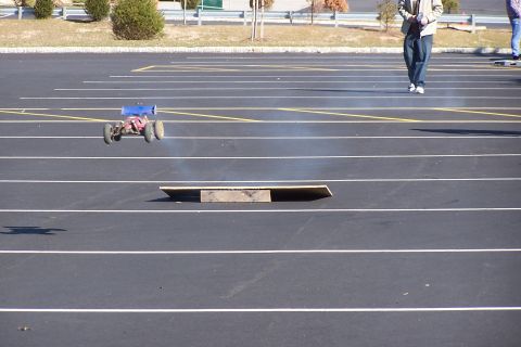1994 Ford Bronco - A remote control car jumps over a ramp in a parking lot.