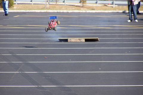1994 Ford Bronco - A remote control car is captured mid-air as it jumps over a ramp on a paved surface.