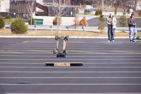 1994 Ford Bronco - A remote control car is captured mid-air, upside down, after launching from a ramp in a parking lot.