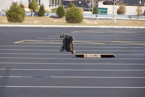 1994 Ford Bronco - An RC car is captured mid-flip after launching off a makeshift ramp in an empty parking lot.