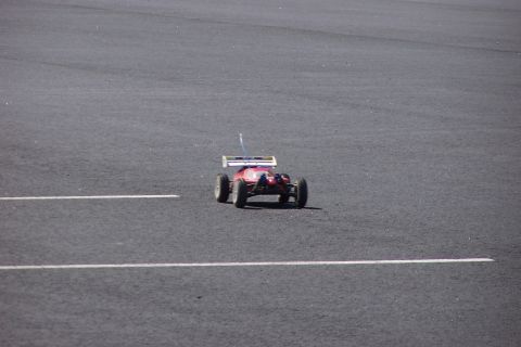 1994 Ford Bronco - A small, red remote-controlled car with a spoiler sits on a paved track with white lines.