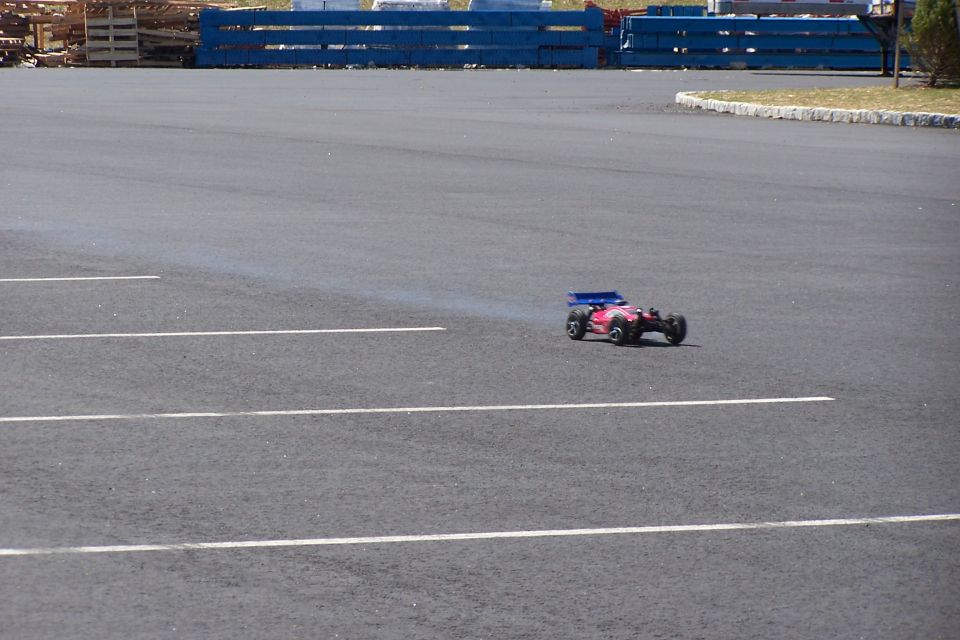 Remote control car with blue spoiler on asphalt lot, emitting smoke