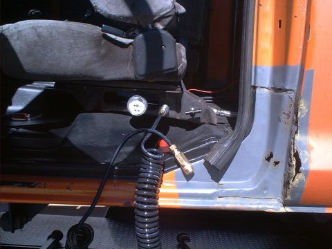 1978 Ford Bronco - The interior of an orange vehicle reveals a pressure gauge and a coiled hose, with significant rust on the door frame.