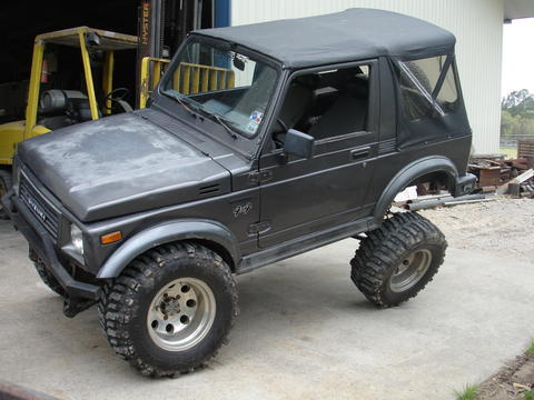 1987 Ford Bronco - Suzuki Samurai modified with large tires and lifted suspension sits on a concrete surface.