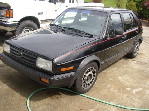 1987 Volkswagen Golf - A black 1987 Volkswagen Golf with distinctive red pinstripes is parked on a concrete driveway, with a white truck visible in the background.