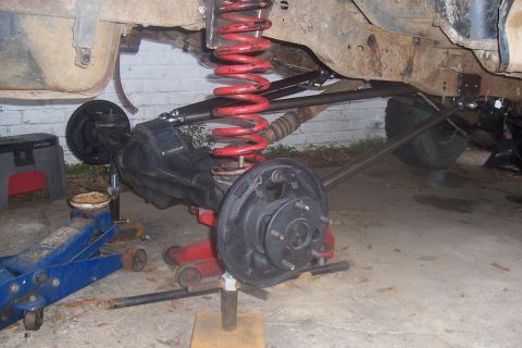 1987 Ford Bronco - The rear suspension and axle assembly of a vehicle are visible, supported by jacks and undergoing modification.