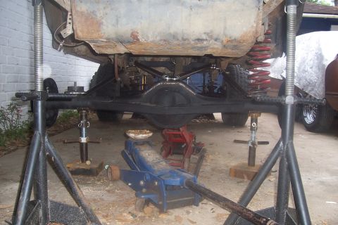 1987 Ford Bronco - The rear axle and suspension components of a vehicle are visible while it is supported by jack stands.