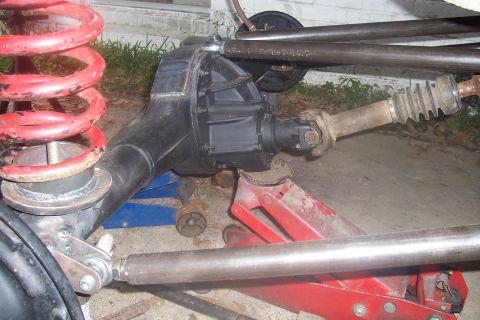 1987 Ford Bronco - Close-up view of a vehicle's rear axle and suspension system, showing a red coil spring and various linkage components.