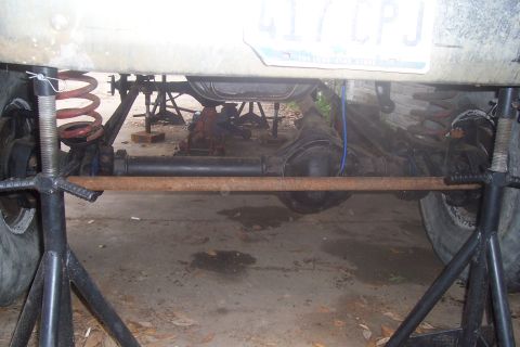 1987 Ford Bronco - The underside of a vehicle is supported by jack stands, revealing its suspension components and rear axle.