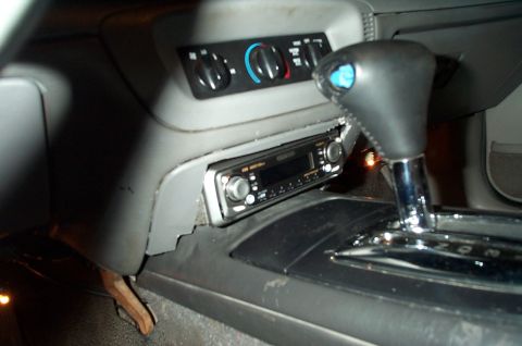 1999 Ford Crown Victoria - Interior center console of a vehicle showing an aftermarket single-DIN car stereo mounted below the round HVAC climate control knobs, with…