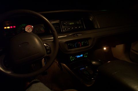 1999 Ford Crown Victoria - Nighttime interior shot of a Ford sedan showing the illuminated dashboard, with the Ford-logo steering wheel, gauge cluster, a round white…