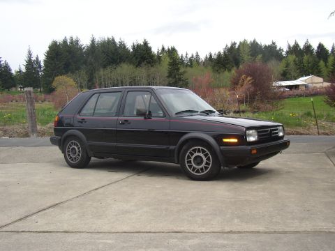 1987 Volkswagen Golf - This 1987 Volkswagen Golf is parked outdoors with a wooded area and house visible behind it.
