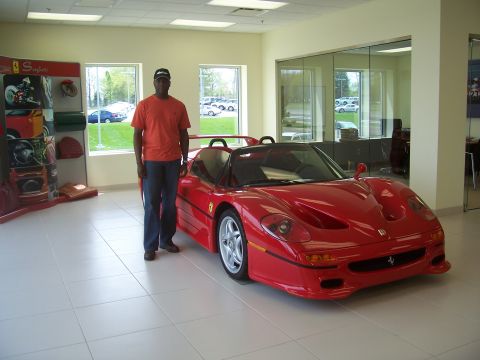 1978 Ford Bronco - A man poses with a red Ferrari F50 in a dealership showroom.