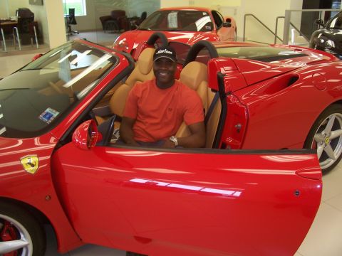 1978 Ford Bronco - A man sits inside a red convertible sports car, with another red car visible in the background.