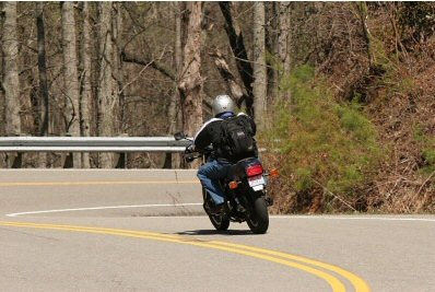 1985 Ford LTD Crown Victoria - Motorcyclist navigates a curve on a tree-lined road.