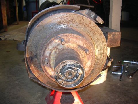 1991 Ford Bronco - A close-up view of a heavily rusted brake rotor and hub assembly, supported by a red jack stand.