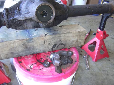 1991 Ford Bronco - A vehicle's axle housing and a knuckle are shown disassembled, resting on a bucket and supported by jack stands.