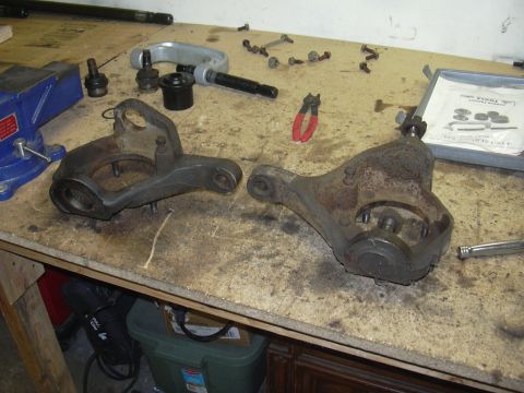 1991 Ford Bronco - Steering knuckle parts and tools laid out on a workbench, likely for a vehicle repair or rebuild.