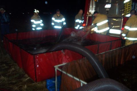1998 Ford Crown Victoria - Firefighters are seen filling a portable water tank from a truck at night.