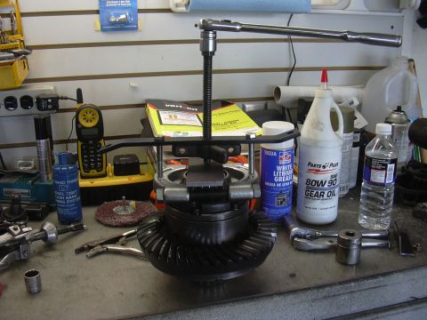 1991 Ford Bronco - A differential gear assembly is being worked on with a puller tool, surrounded by lubricants and tools on a workbench.