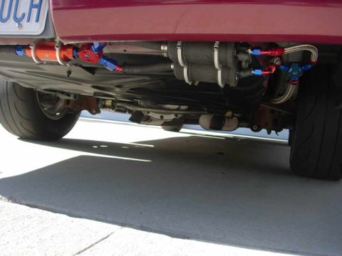 1992 Ford Crown Victoria - The underside of a red vehicle displays aftermarket fuel system components and a license plate.