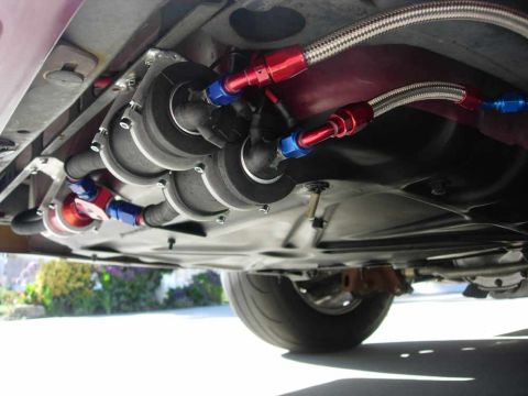 1992 Ford Crown Victoria - Underbody view of a custom fuel system on a maroon car, with a pair of large inline fuel pumps bracketed to the floor pan and joined by bra…