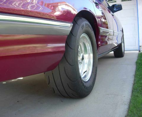 1992 Ford Crown Victoria - Low-angle close-up of the rear quarter of a dark maroon/burgundy sedan, showing a polished aluminum wheel fitted with a Mickey Thompson ET…